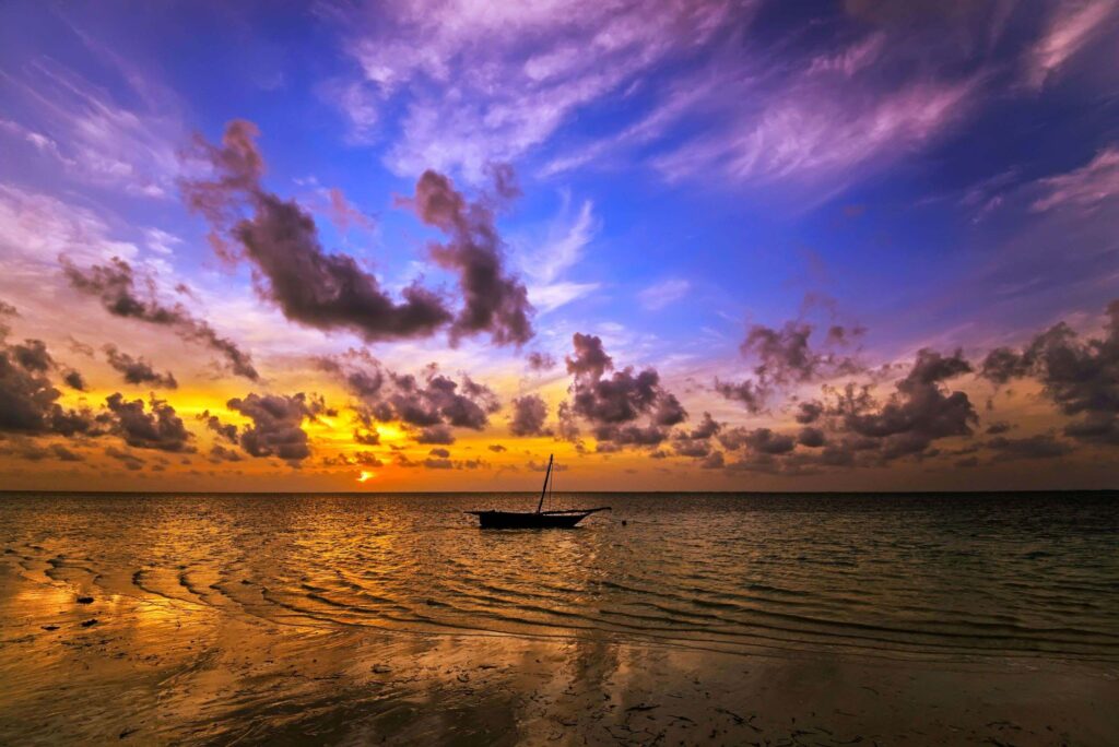 Boat on Indian Ocean with the sun setting in the background and clouds in the purple sky