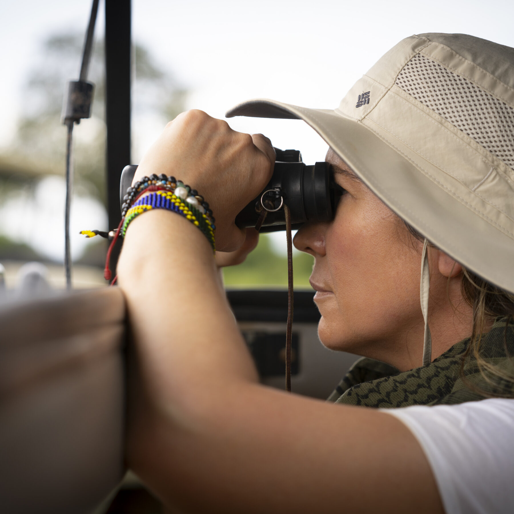 Woman with a hat and binoculars looking out from a car in Serengeti