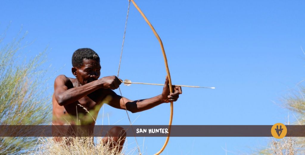 San Bushman with bow and arrow on a hill with some grass in front