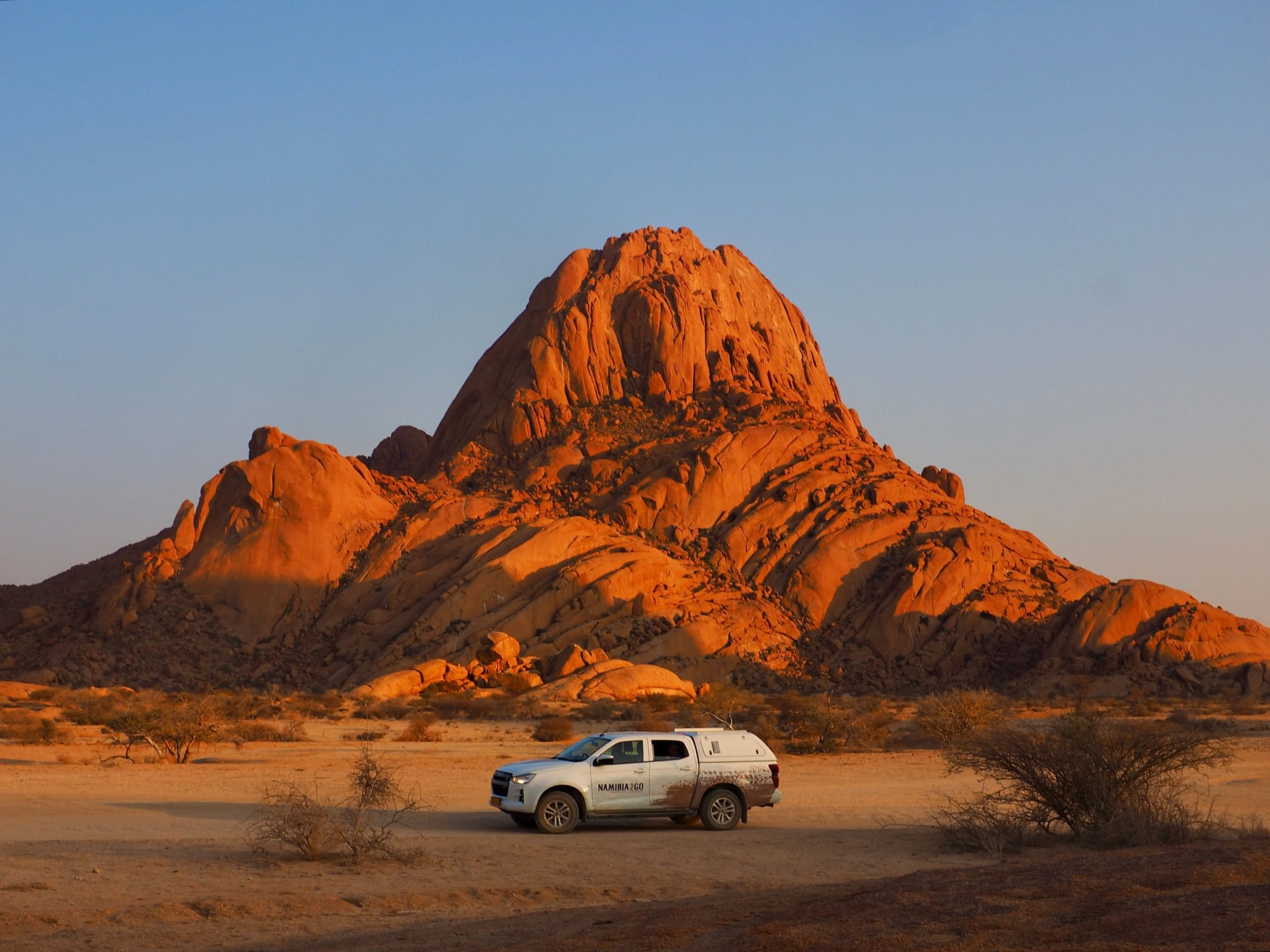Safari vehicle parked below Spitzkoppe in sunset